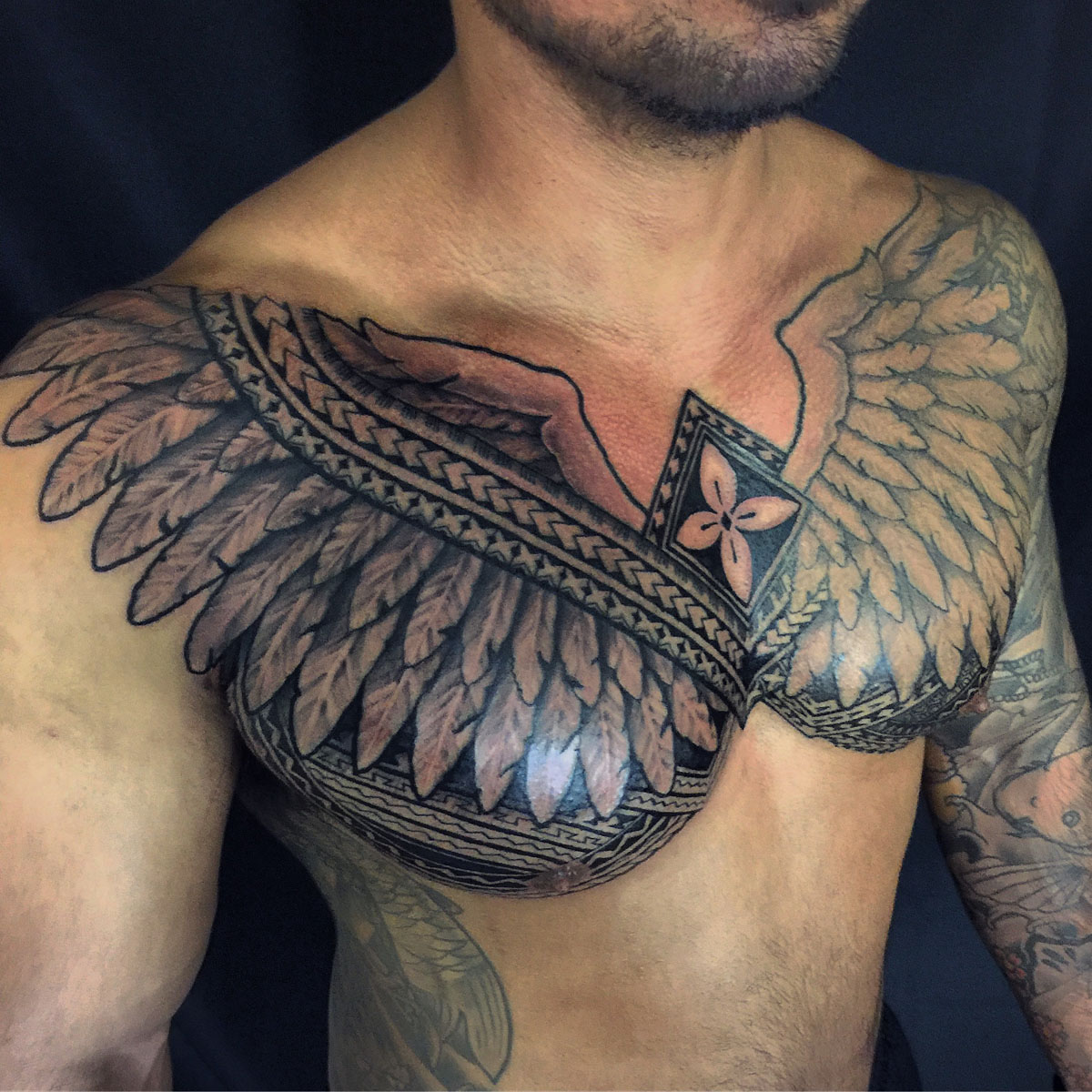 Chest and shoulder tattoo combining feather forms with geometric bands